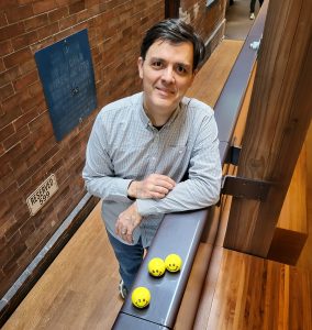 Portrait of Adriano Macedo with three smiley face stress balls at the ramp railing of Max Gluskin House