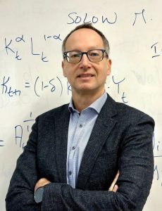 Portrait of Professor Diego Restuccia in front of a mathematical formula written on a white board. 