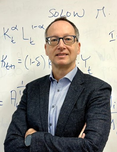 Portrait of Professor Diego Restuccia in front of a mathematical formula written on a white board.